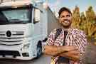 Ein Mann steht lächelnd neben einem LKW. 